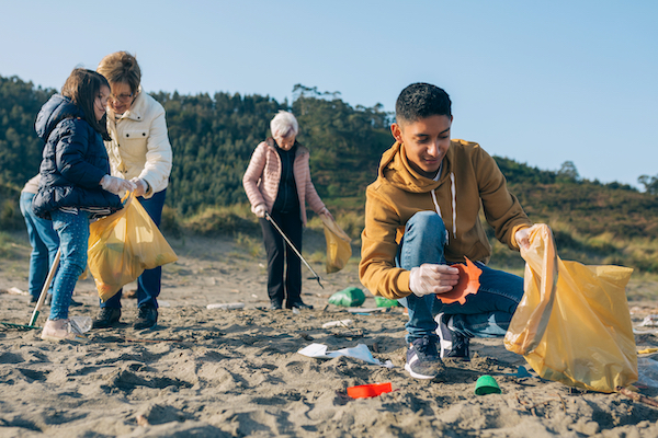 Young,Man,Picking,Up,Trash,With,Group,Of,Volunteers,On